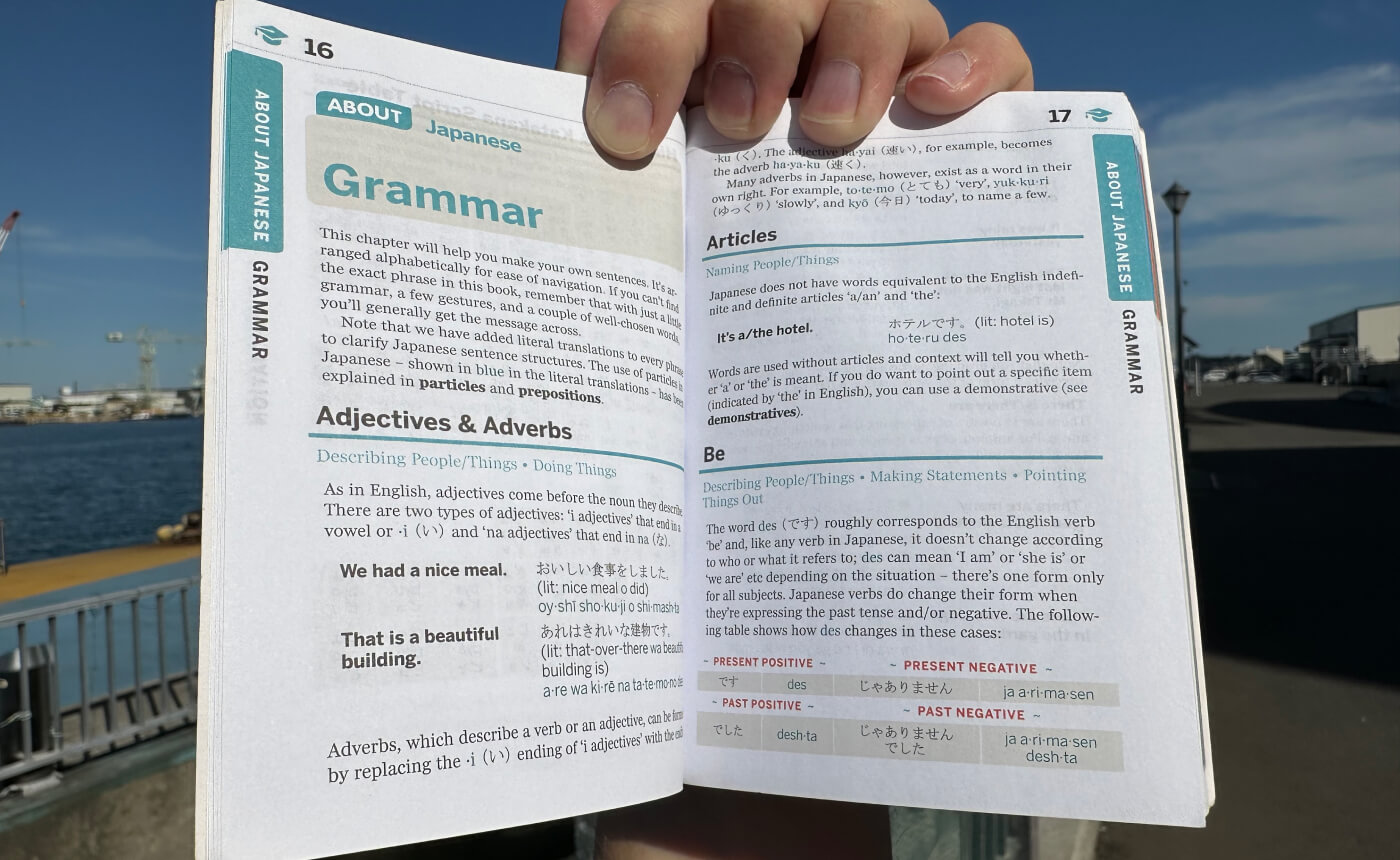 Hand håller i en liten bok. Två sidor syns. Innehållet handlar om grammatik som adjektiv och adverb.