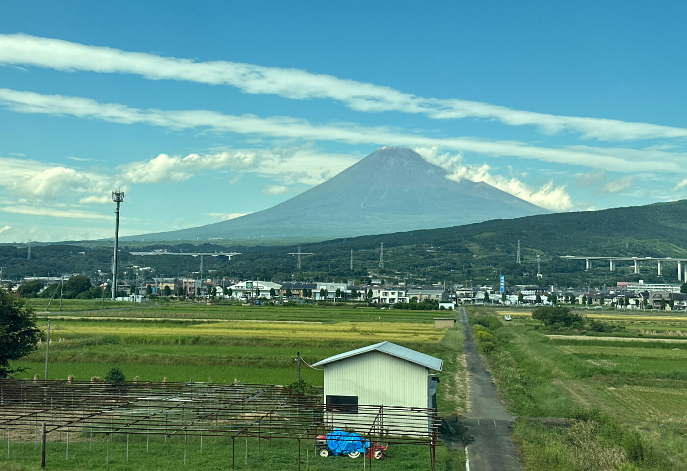 I fjärran Japans högsta berg Mount Fuji. I förgrunden ett plåtskjul. I mitten ett bostadsområde.