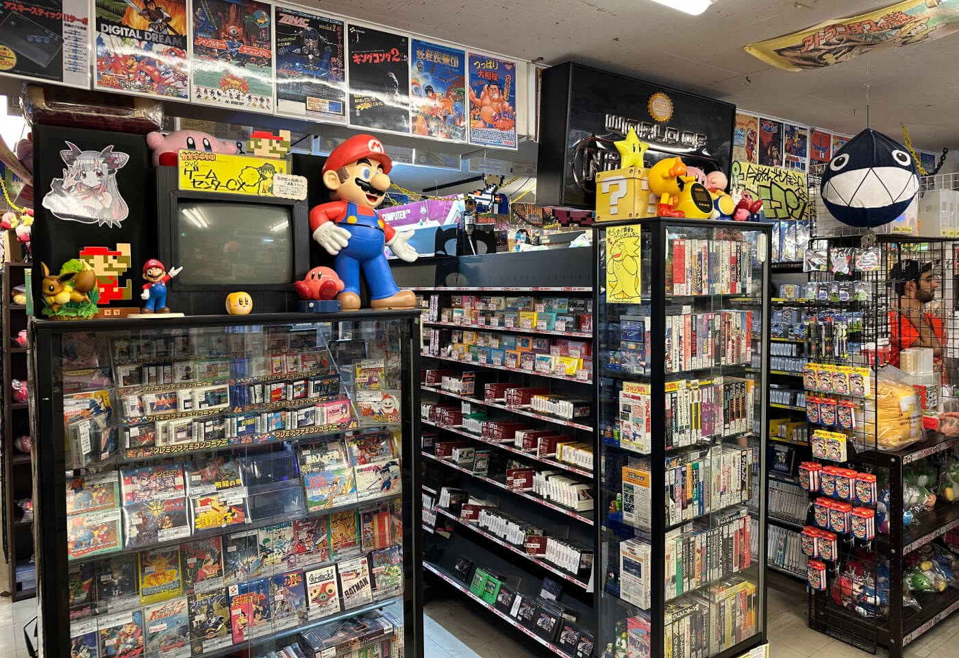 Flera rader med butikshyllor fyllda med gamla TV-spel. Ovanpå hyllorna finns plastfigurer på bland annat Super Mario.