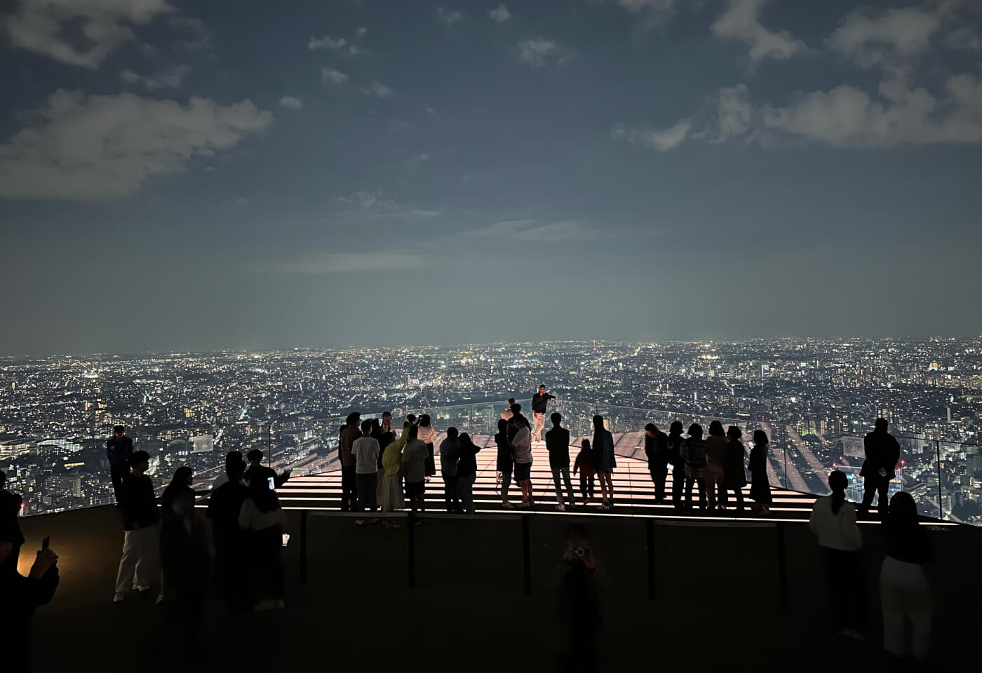 Upplyst sektion på öppen utkiksplats över Tokyo på kvällstid. Personer står i kö för att ta bild på sektionen.