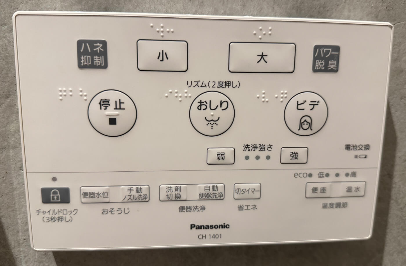 Vit väggdosa för att styra en japansk toalett. Dosan har femton knappar och bara text på japanska. Vissa knappar har ikoner.