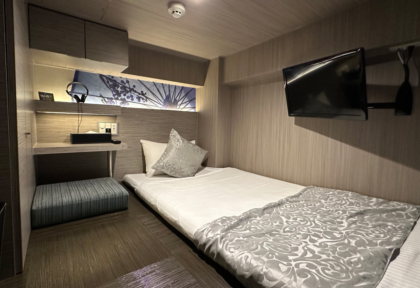 Litet hotellrum med lågt till tak. Till höger en madras med täckte och kudde-. Till vänster ett litet bord och en sittkudde.