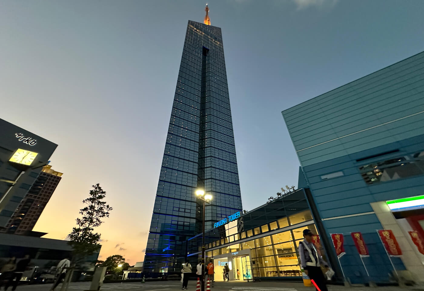 Utkikstornet Fukuoka Tower sett från marken. I bakgrunden kan man ana solnedgången.