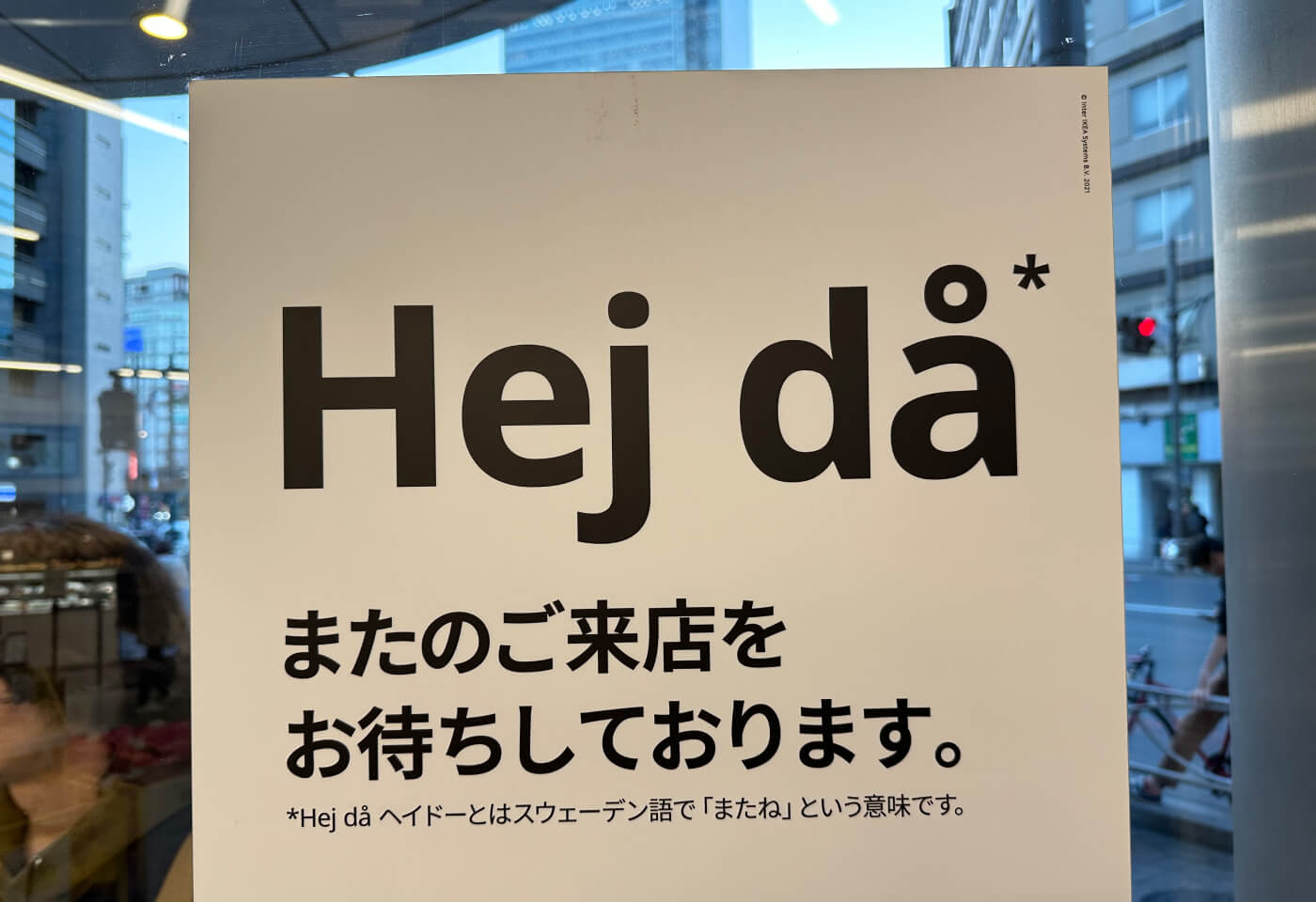 Skylt på fönster med texten "Hej då" följt av japansk skrift.