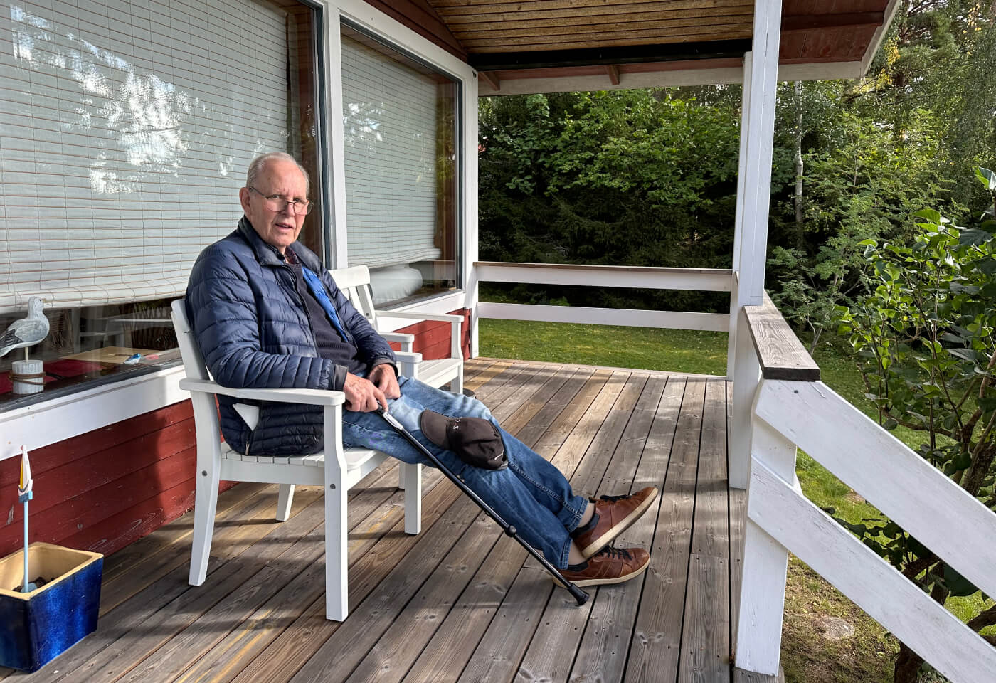 Min pappa sture sitter på en vit stol på en terass under tak. Han har blåa kläder på sig och tittar in i kameran.