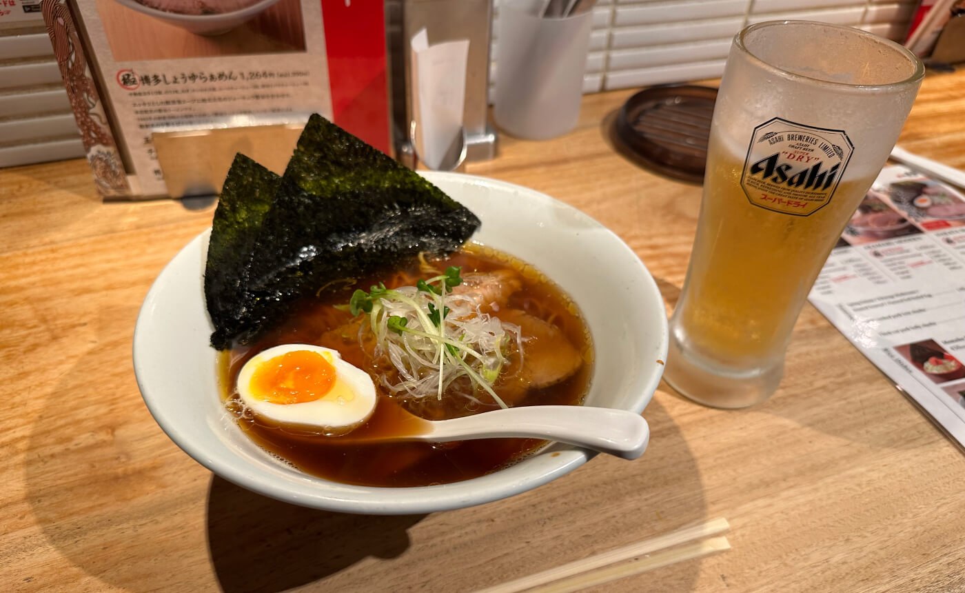 En vit skål med ramen inklusive ett halvt kokt ägg. Till höger ett stop öl.